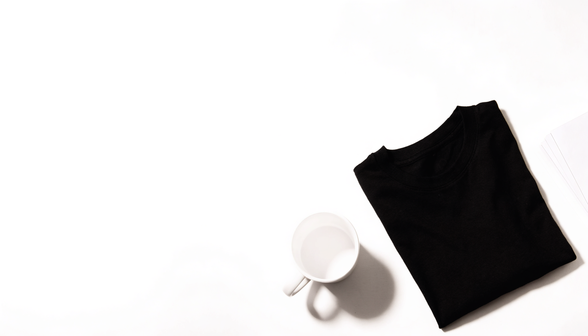 Polera negra doblada, taza blanca y láminas impresas sobre fondo blanco